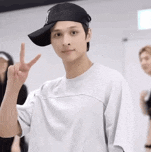 a young man wearing a baseball cap and a white shirt is giving a peace sign .