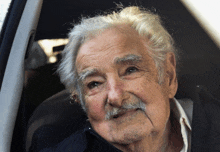 a man with gray hair and a mustache is sitting in the back seat of a car