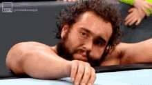 a man with a beard is laying on a wrestling mat with his head on the mat .