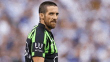 a man with a beard is wearing a green and black striped shirt with the word witzer on the sleeves .
