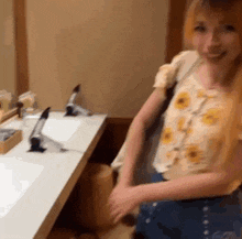 a woman in a floral shirt is standing in front of a bathroom sink .