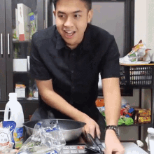 a man in a black shirt is preparing food in a kitchen with a bag of tofu plus on the counter