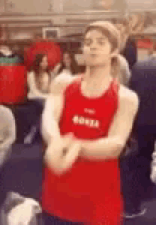 a man in a red tank top is standing with his arms crossed in a crowded room .