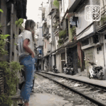 a woman is standing on a sidewalk next to train tracks