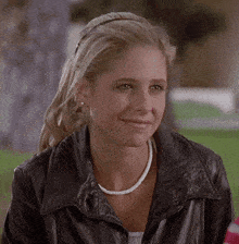 a woman wearing a black leather jacket and a white necklace smiles for the camera