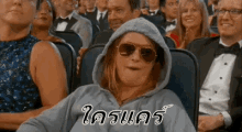 a woman wearing sunglasses and a hoodie is sitting in a crowd of people in a theater .