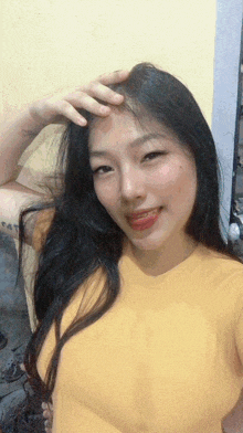 a woman in a yellow shirt is taking a selfie with her hand on her forehead