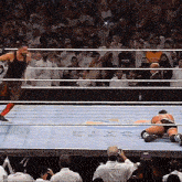 a man in a tank top is standing in a wrestling ring with a crowd watching .