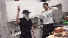 two men are dancing in a kitchen with one wearing a bandana