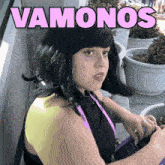 a woman in a black wig stands in front of a sign that says " vamos "