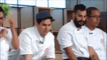 a group of men are sitting in a room and one of them is wearing a hat .