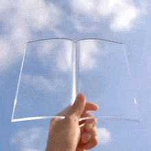 a person is holding a clear book in their hand against a blue sky .