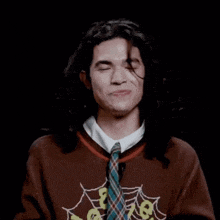 a man with long hair is wearing a sweater and tie and making a face .