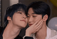 two young men are touching each other 's faces and one of them is putting his hand on the other 's face .