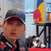 a man wearing a hat and a red bull shirt is looking at the camera .