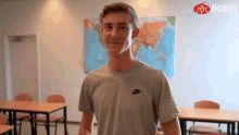 a man in a grey nike shirt stands in front of a map of the world