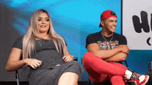 a man and a woman are sitting next to each other with their arms crossed in front of a sign that says hi
