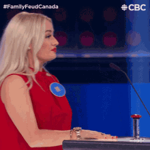 a woman in a red dress is sitting at a table with a microphone and pressing a button .