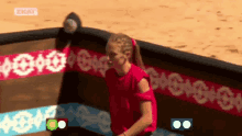 a woman in a red shirt is standing in front of a barrier on a sandy beach .