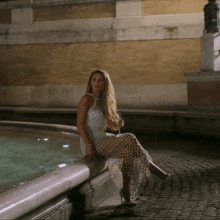 a woman in a white dress sits on the edge of a fountain holding a glass of wine