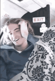 a man is sitting in front of an exit sign on a plane .