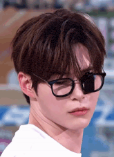 a young man wearing glasses and a white shirt looks at the camera