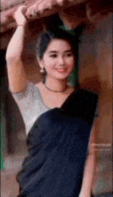 a woman in a black saree is standing on a roof with her hand in her hair .