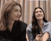 two women are sitting next to each other and one is holding a small object