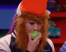 a woman with red hair is eating an apple while wearing an orange hat .