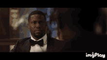 a man in a tuxedo is looking at another man in a dark room with imgplay at the bottom of the screen