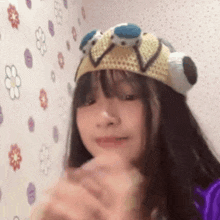 a girl wearing a hat with a frog on it is standing in front of a wall with flowers on it .