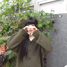 a woman in a green sweater making a heart with her hands