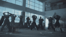 a group of people are standing in a room with a lot of windows