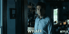 a man in a blue shirt is standing in front of a door and says what