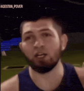 a man with a beard is wearing a blue tank top and looking at the camera .