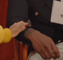 a woman 's hand rests on a man 's arm with a yellow sweater in the background