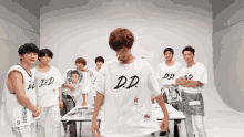 a group of young men wearing white shirts with d.d. on them stand around a table