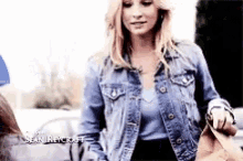a woman wearing a denim jacket is standing next to a man holding a purse .
