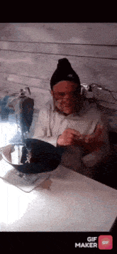 a man is sitting at a table with a sewing machine and a gif maker button on the bottom right