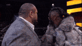 a man in a fur coat talks to another man in a suit on a tv screen that says live