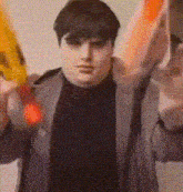 a man is holding two nerf guns in his hands while wearing a black shirt and a gray jacket .
