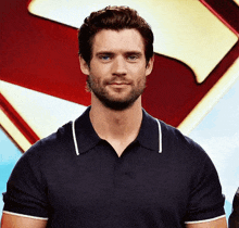a man with a beard wearing a blue polo shirt is smiling in front of a superman logo .