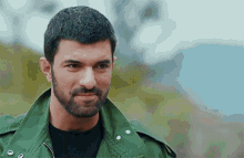 a man with a beard and a green jacket is smiling .