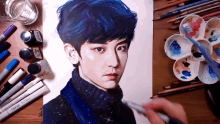 a drawing of a boy with blue hair is on a table with markers and paints