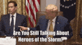 a man in a suit and tie is pointing at a sign that says are you still talking about heroes of the storm ?