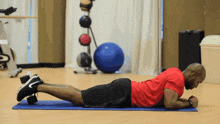 a man in a red shirt is doing a plank on a mat
