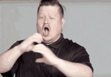 a man is making a heart shape with his hands while wearing a black shirt .