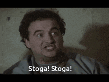 a man in a hospital gown is making a funny face and says stoga stoga .