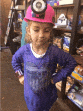 a little girl wearing a pink hard hat with a light on it