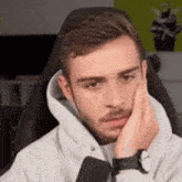 a man is sitting in a chair with his hand on his face and a watch on his wrist .
